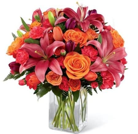  Brilliant orange roses, spray roses and tulips are simply stunning arranged amongst hot pink mini carnations, purple tulips, dark pink Asiatic lilies and lush greens. Presented in a designer rectangular clear glass vase,