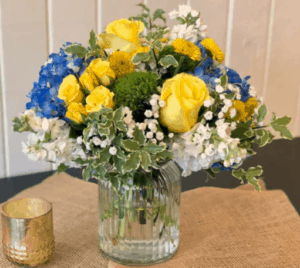 Blue yellow and white flowers to include a few roses in a clear vase.