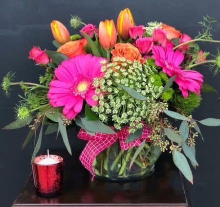 Bright pink and orange tones in a cylinder vase with a bright pink ribbon
