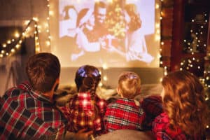 happy family in checkered pajamas: mother father and children watching projector, film, movies with popcorn in christmas holiday evening at home